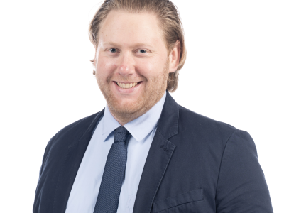 Headshot of Jacob Richter against a white background. He is wearing a black suit with a light blue shirt and dark blue tie.