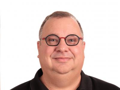 A headshot of Zak Wolfe wearing black against a white background.