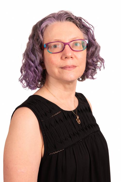 Headshot of Carol Hayes in a black shirt with a white background. Her hair is purple and very cool.