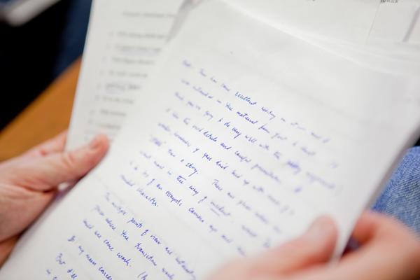 A hand holding a stack of papers with writing on them