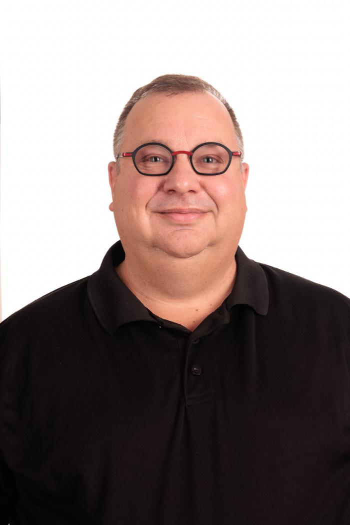 A headshot of Zak Wolfe wearing black against a white background.