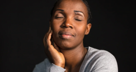 Black woman faces camera, eyes closed, hand resting on cheek.