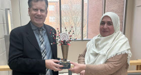 Dr. Nabila Hijazi and Dr. Mark Mullen face the camera, holding a trophy between them.
